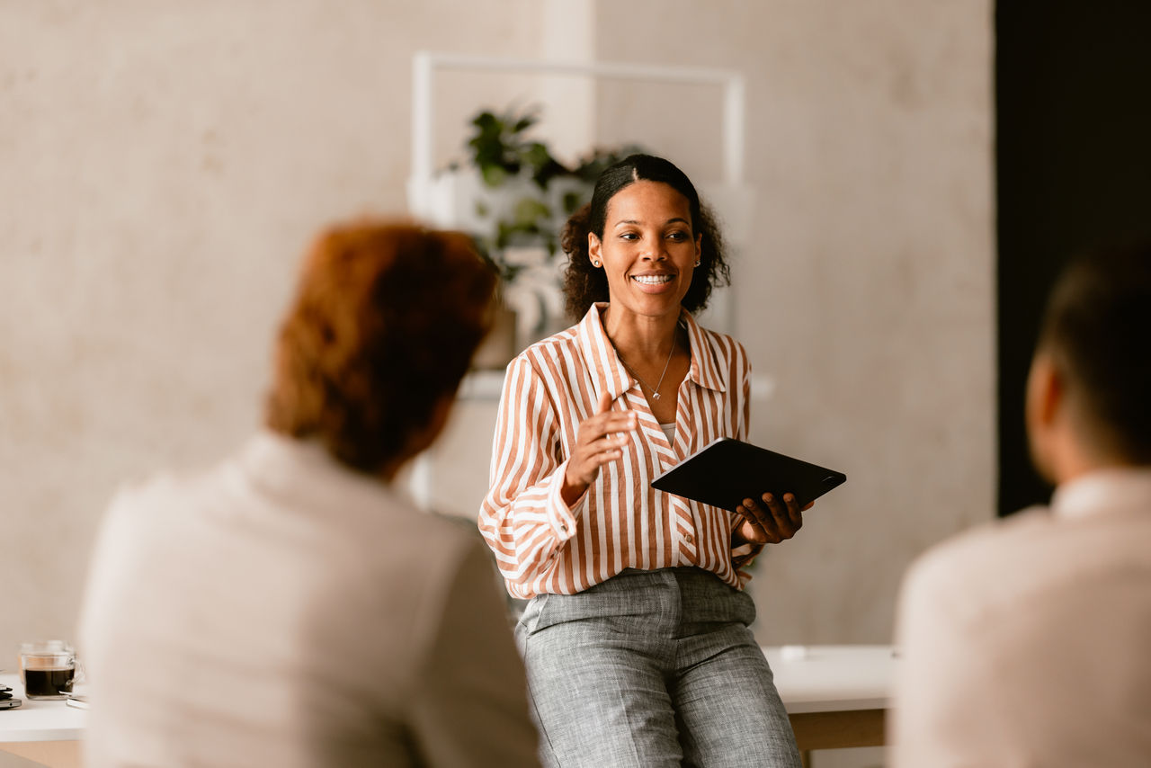 Confident businesswoman leading a group business meeting at a bright beige office. Professional interaction and teamwork concept.