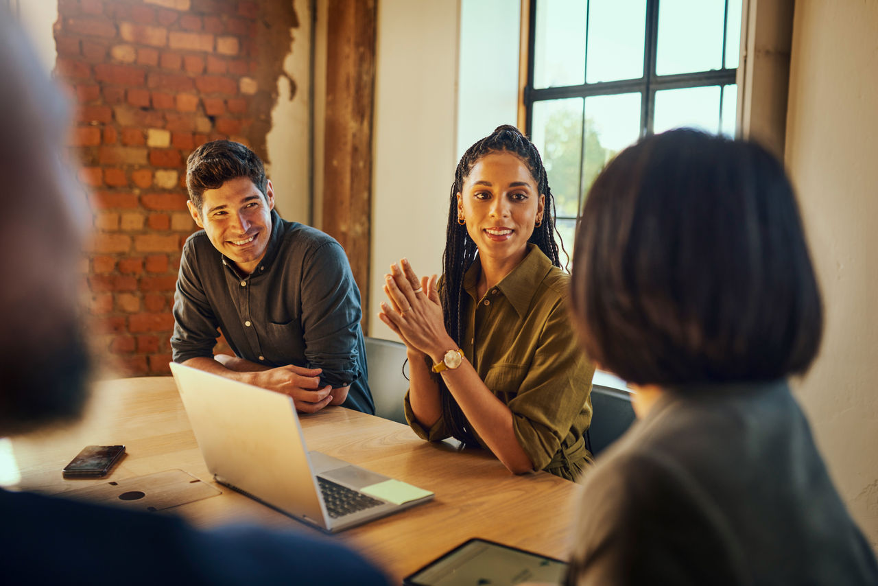 Cheerful businesswoman, clasping hands, smiling at client at meeting table in boardroom