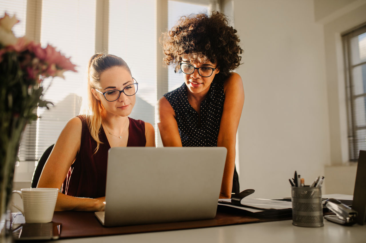 Portrait of two businesswomen looking at laptop and discussing new project in office. Young business colleagues discussing work in the office.